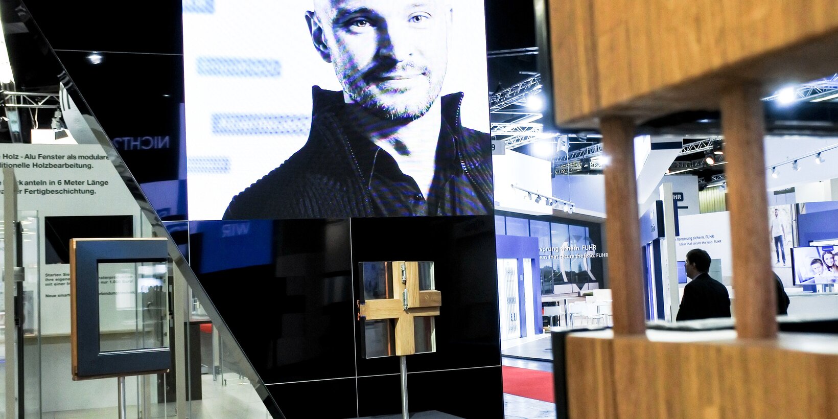 Ausschnitt des Messestands mit einer Screenleinwand und zwei Fensterexponaten