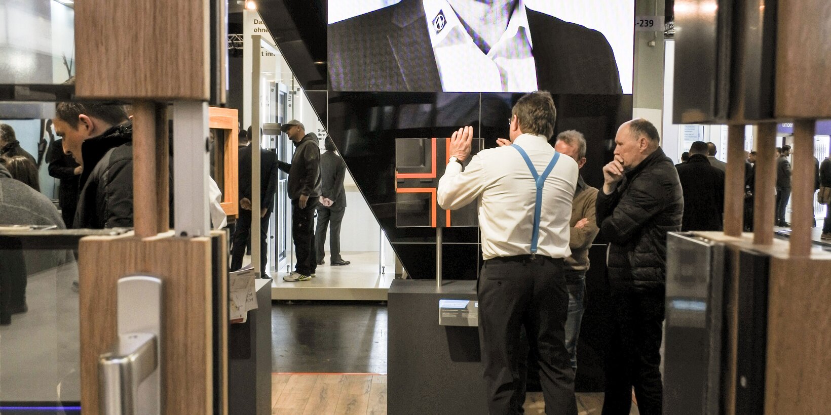Ein BUG Mitarbeiter erklärt zwei Personen das Exponat im Vordergrund der Screen Leinwand