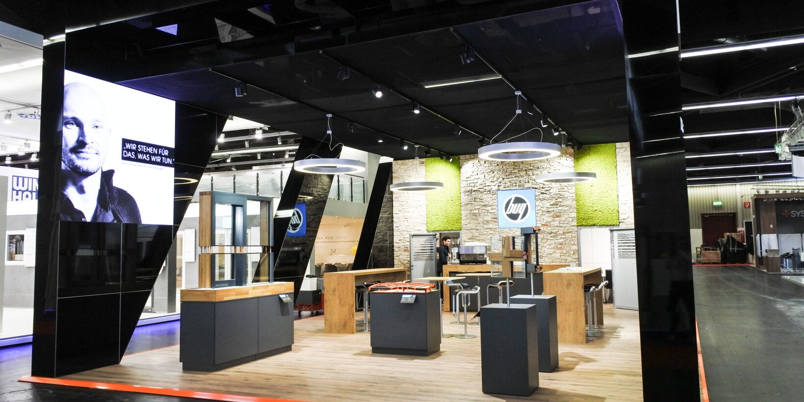 Front view of the black exhibition booth with four window samples and a lounge area