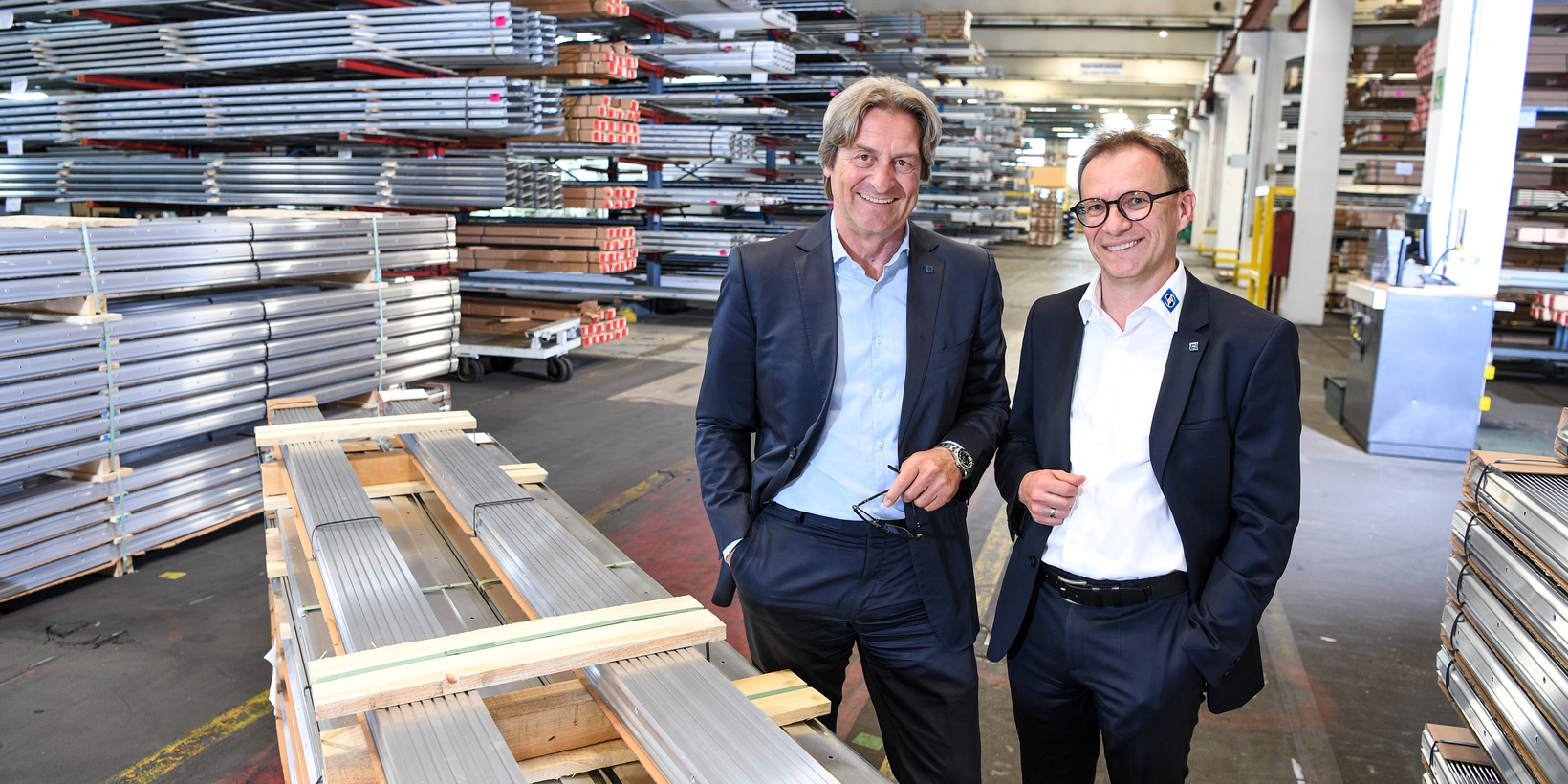 Zwei Personen umgeben von Aluminiumprofilen in einer Halle