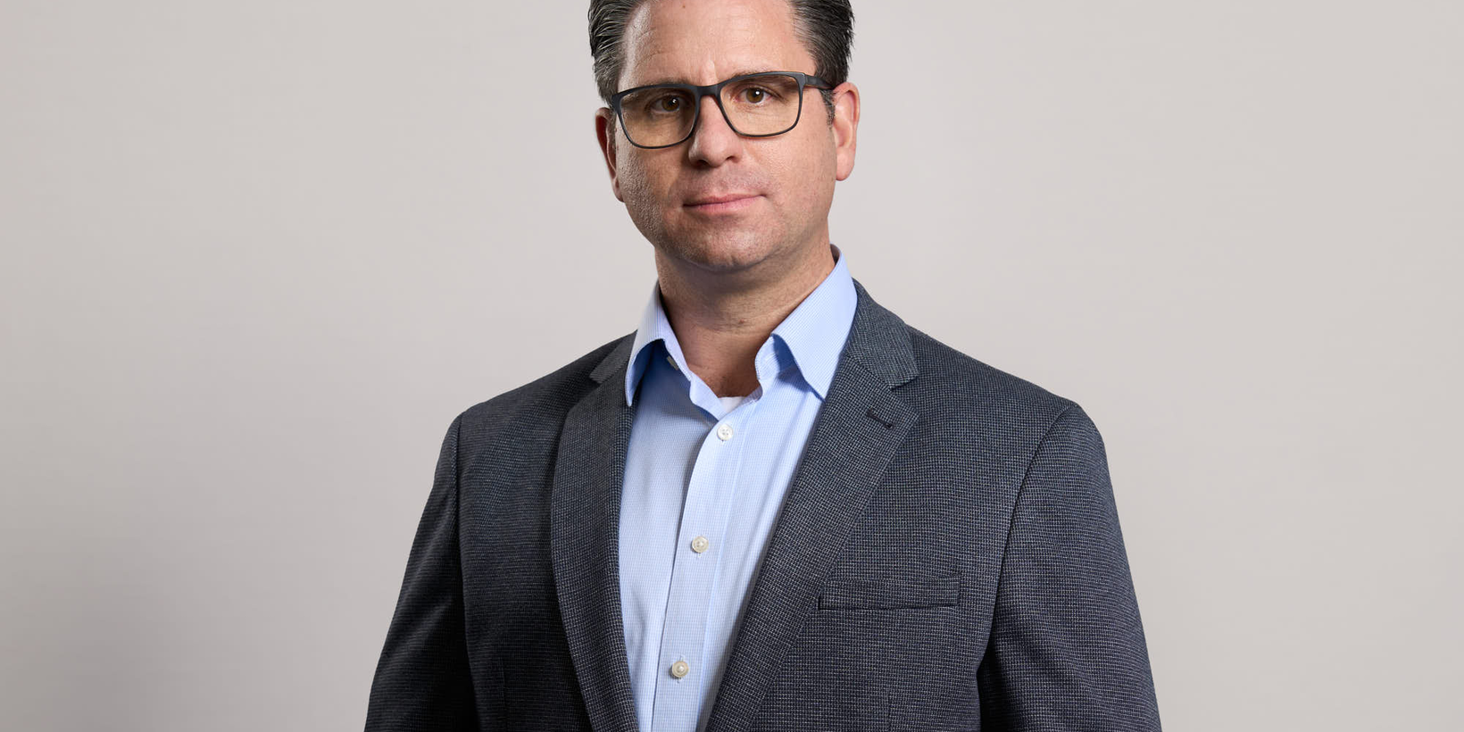 Portraitbild einer männlichen Person mit Brille im grauen Anzug mit hellblauem Hemd vor hellgrauem Hintergrund