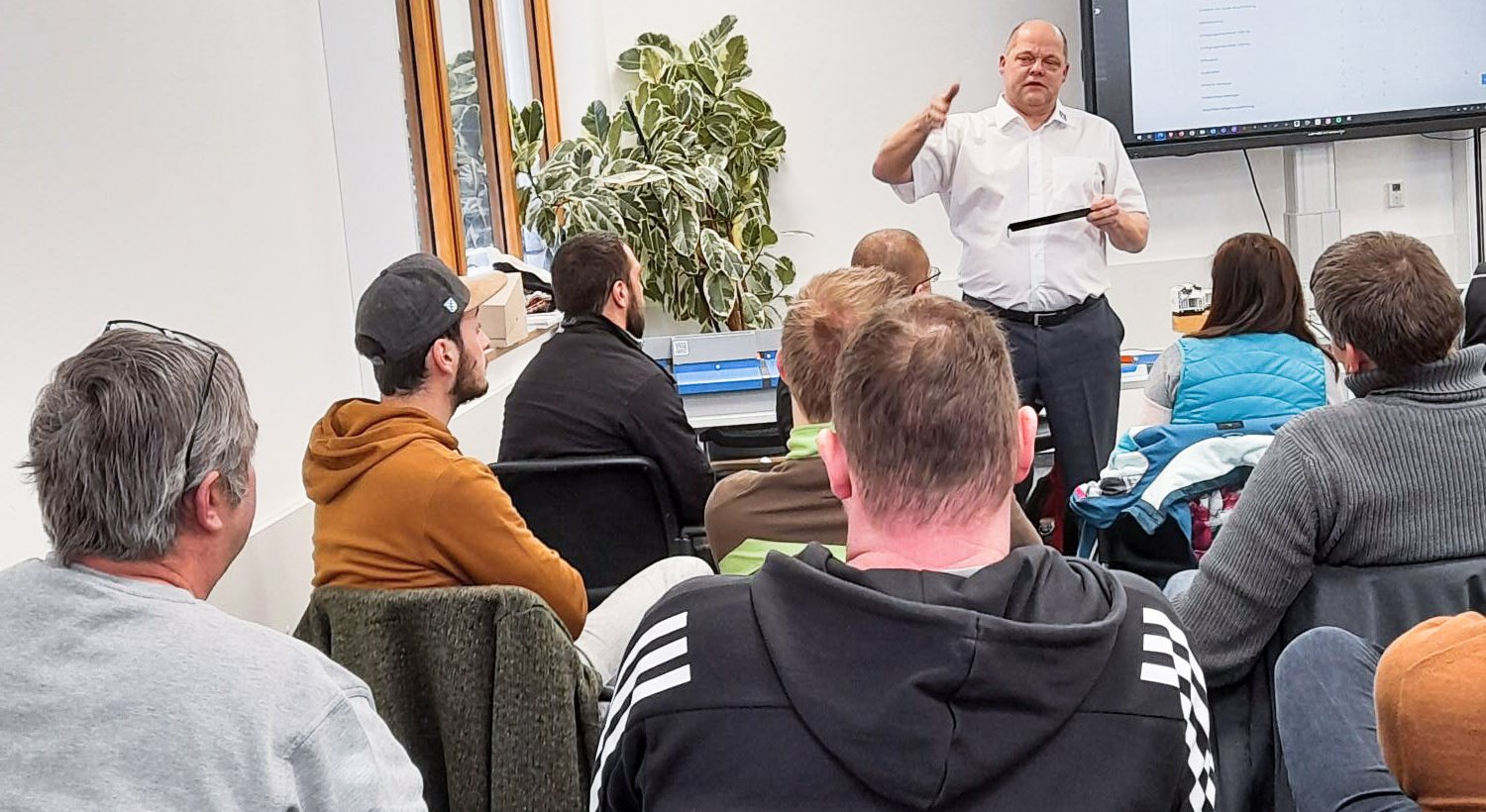 Mann in weißem Kurzarmhemd hält einen Vortrag vor einer Gruppe mit neuen Personen